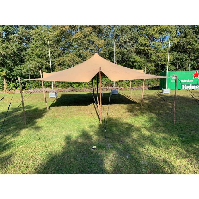 een stretchtent van 6x6 meter zit met houten palen vast in de grond. Er staat één paal in het midden om de gehele tent omhoog te houden. de houten palen zijn vastgezet met touwen en haringen die in de grond zitten.