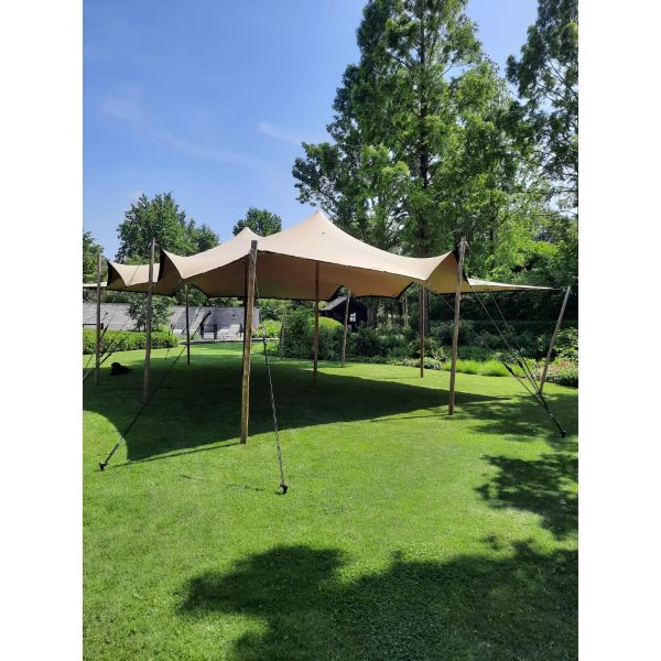 een stretchtent van 7,5x10,5 meter zit met houten palen vast in de grond. Er staan twee palen in het midden om de gehele tent omhoog te houden. de houten palen zijn vastgezet met touwen en haringen die in de grond zitten.