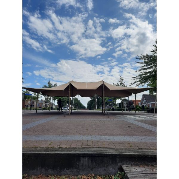 een stretchtent van 10,5x12 meter zit met houten palen vast in de grond. Er staan twee palen in het midden om de gehele tent omhoog te houden. de houten palen zijn vastgezet met touwen en haringen die in de grond zitten.
